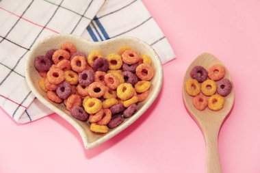 kupkuru çocukların kahvaltısı çok renkli halkalar seramik tabakta kalp şeklinde ve ahşap bir kaşıkta pembe arka planda