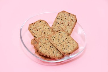 Siyah kimyon tohumlu kuru kare diyet krakerleri ve pembe arka planda şeffaf cam bir tabakta kinoa.