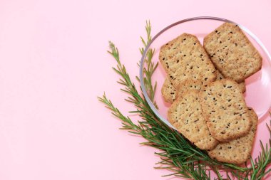 Siyah kimyon tohumlu kuru kare diyet krakerleri ve pembe arka planda şeffaf cam bir tabakta kinoa.