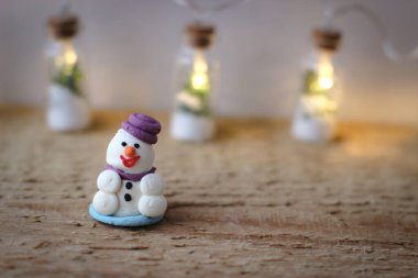 Noel dekoru. Mor şapkalı pudra şekerli bir kardan adamın minyatür figürü tahta bir tahtanın üzerinde duruyor..