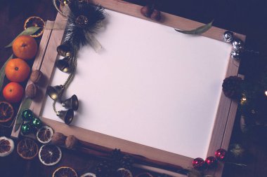 Noel maketi. Merkezde, Noel elfleri, portakallar, çanlar ve çelenkler etrafında ahşap çerçeveli beyaz bir masa var..