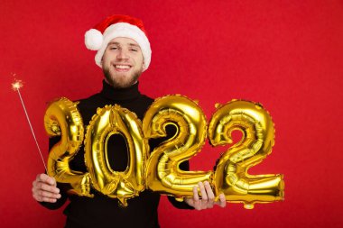 Noel Baba şapkalı bir adam 2022 rakamlarını ve maytap taşır.