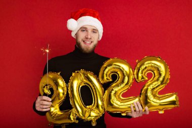 Noel Baba şapkalı bir adam 2022 rakamlarını ve maytap taşır.