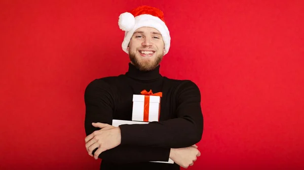 サンタクロースの帽子の幸せな男の肖像とギフトボックス赤い背景 — ストック写真