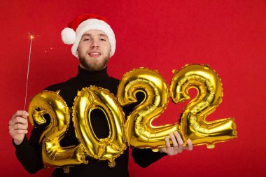 Noel Baba şapkalı bir adam 2022 rakamlarını ve maytap taşır.