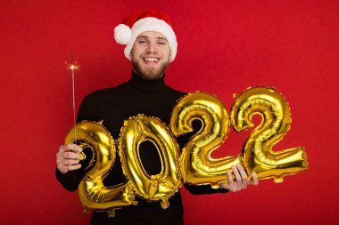 Noel Baba şapkalı bir adam 2022 rakamlarını ve maytap taşır.