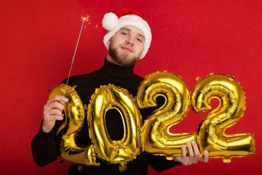 Noel Baba şapkalı bir adam 2022 rakamlarını ve maytap taşır.