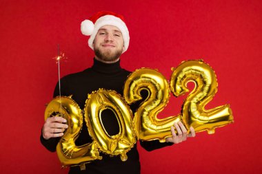 Noel Baba şapkalı bir adam 2022 rakamlarını ve maytap taşır.