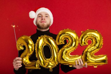 Noel Baba şapkalı bir adam 2022 rakamlarını ve maytap taşır.