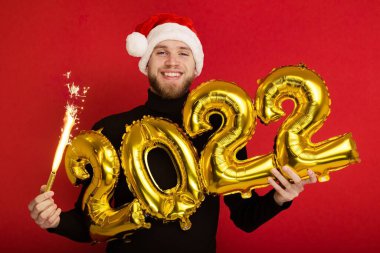 Noel Baba şapkalı bir adam 2022 rakamlarını ve maytap taşır.