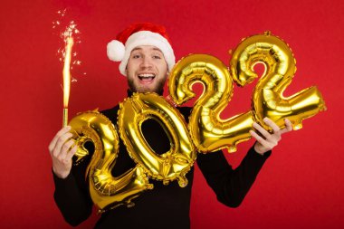 Noel Baba şapkalı bir adam 2022 rakamlarını ve maytap taşır.
