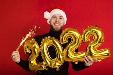 Noel Baba şapkalı bir adam 2022 rakamlarını ve maytap taşır.