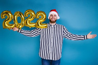 Noel şapkalı bir adam şişme balonlardan 2022 rakamlarını saklar.
