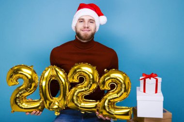 Kırmızı şapkalı bir adam 2022 yılının rakamlarını taşıyor. Hediyelerle dolu kutular yakında.
