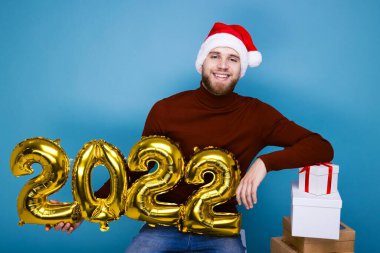 Kırmızı şapkalı bir adam 2022 yılının rakamlarını taşıyor. Hediyelerle dolu kutular yakında.