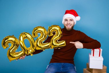 Kırmızı şapkalı bir adam 2022 yılının rakamlarını taşıyor. Hediyelerle dolu kutular yakında.