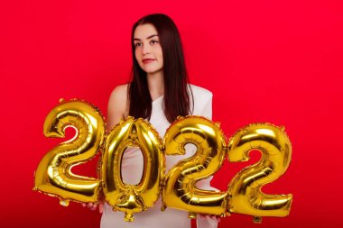 Noel tatili - Beyaz elbiseli genç bir kadın kırmızı arka planda 2022 rakamlarını tutuyor