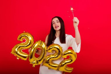 Noel Tatili Konseri. Üzerinde 2022 rakamları ve maytap taşıyan beyaz elbiseli, gülümseyen bir kadın.