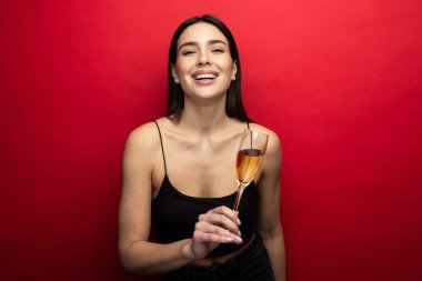 Kırmızı arka planda bir bardak şampanyası olan güzel bir esmer
