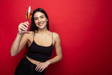 Kırmızı arka planda bir bardak şampanyayla gülümseyen esmer