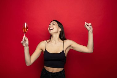 Kırmızı arka planda bir bardak şampanyayla gülümseyen genç kadın.