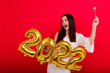 Noel Tatili Konseri. Üzerinde 2022 rakamları ve maytap taşıyan beyaz elbiseli, gülümseyen bir kadın.