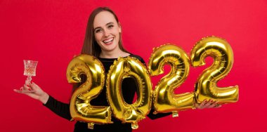 Tatiller, yeni yıl arifesi. Elinde bir bardak şampanya ve 2022 rakamlarıyla siyah elbiseli genç bir kadın.