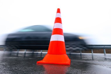 Yoldan geçen bir arabanın arka planında parlak bir trafik konisi