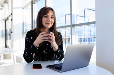 A young woman drinks coffee and works on a laptop in a cafe