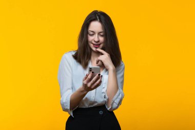 Sarı arka planda telefonu olan beyaz tişörtlü genç bir kadın.