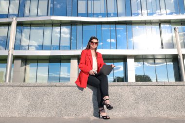 Ceketli bir iş kadını sokakta dizüstü bilgisayarla çalışıyor.