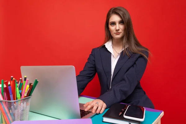 赤い背景のラップトップで働いているビジネス服の若い女性 — ストック写真