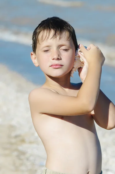 Jongen met shell in hand op het strand — Stockfoto