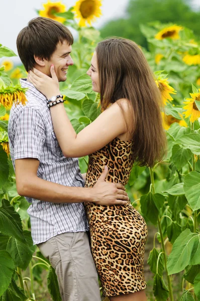 Junges Mädchen und ein junger Mann im Sonnenblumenfeld — Stockfoto