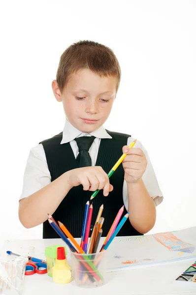 Маленький мальчик за столом с альбомом для рисования, карандаши и книги на белом фоне — стоковое фото