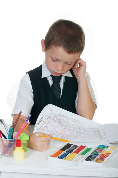 Μικρό αγόρι στο γραφείο του με ένα άλμπουμ για την κατάρτιση, μολύβια και βιβλία σε άσπρο φόντο — Φωτογραφία Αρχείου