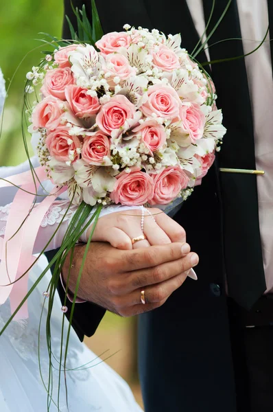 Mariée et marié tenant la main avec des anneaux sur le bouquet floral — Photo