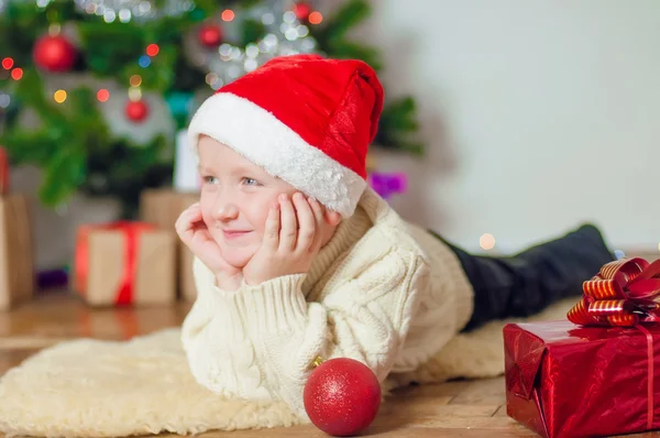 Little boy in santa hat near Christmas tree — Stock Photo, Image