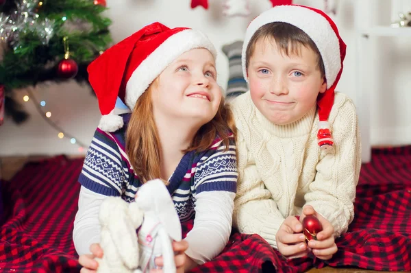Liten pojke och flicka i santa hatt nära julgran med gåvor — Stockfoto