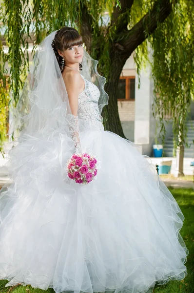 Beautiful bride in wedding dress with a bouquet of flowers on nature — Stock Photo, Image