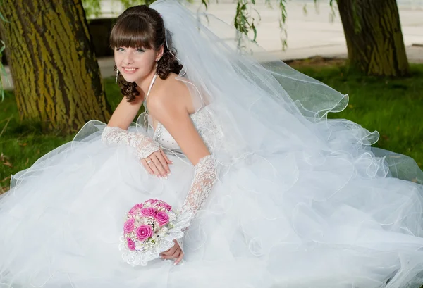 Hermosa novia en vestido de novia con un ramo de flores en la naturaleza — Foto de Stock