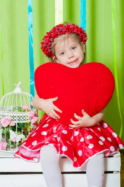Красивая маленькая девочка в красном платье с красной подушкой сердца — стоковое фото