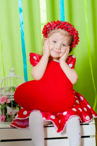 Hermosa niña en un vestido rojo con una almohada de corazón rojo —  Fotos de Stock