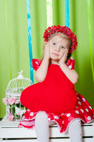 Hermosa niña en un vestido rojo con una almohada de corazón rojo —  Fotos de Stock