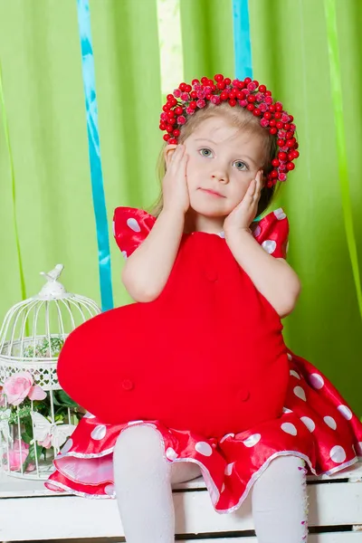 Kırmızı kalp yastık ile Kırmızı elbiseli güzel küçük bir kız — Stok fotoğraf