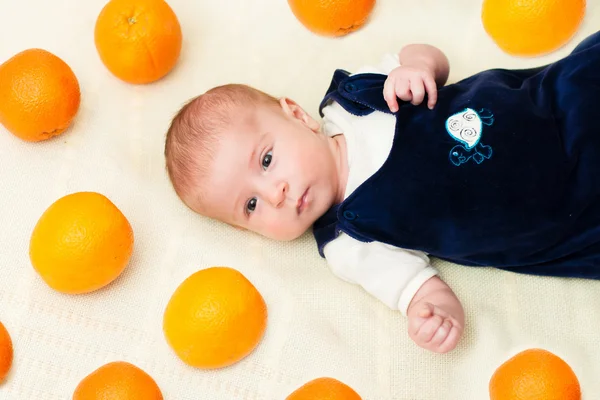 Baby lying on the bed with oranges — Stock Photo, Image
