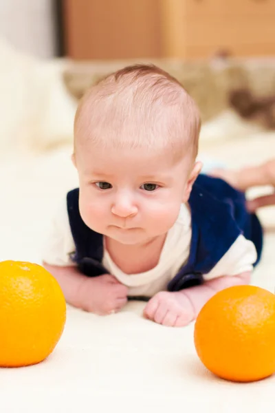 Baby lying on the bed with oranges — Stock Photo, Image