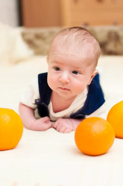 Baby lying on the bed with oranges — Stock Photo, Image