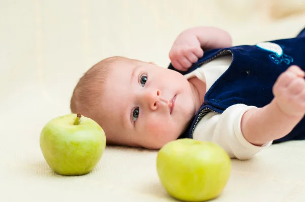Baby lying on the bed with apples — Stock Photo, Image