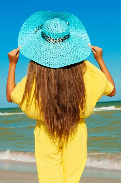 Schönes Mädchen mit langen Haaren am Strand mit blauem Hut — Stockfoto